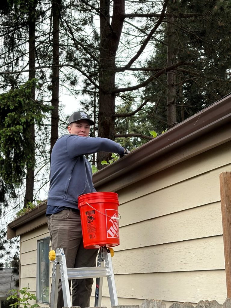 A Solutionist clearing a gutter from a ladder at a South Sound home