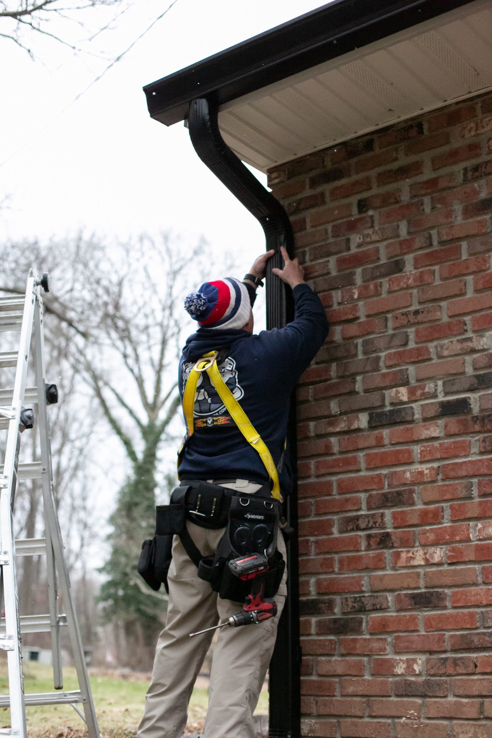 A Brothers that just do Gutters technician installing a downspout on a brick home