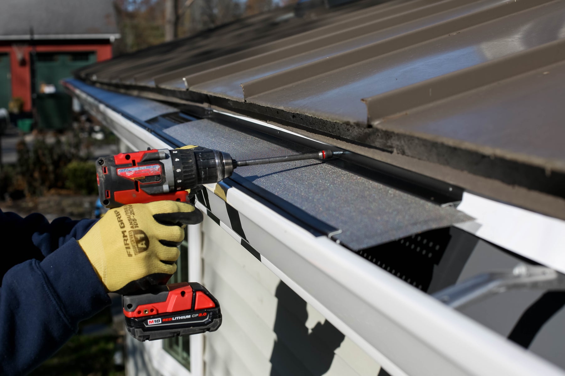 Installer fastening a fine metal mesh gutter guard with a drill